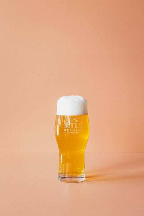 Glass of beer with Brave Brewing Co logo on a peach-colored background
