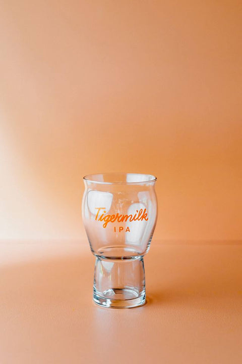 Clear glass with 'Tigermilk IPA' text on a peach background
