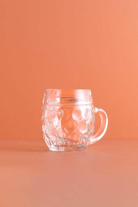 Clear glass Brave Brewing Co lager mug with handle on an orange background