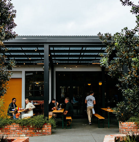 People sitting at outdoor tables under a covered patio area at Brave Brewing Co with greenery.