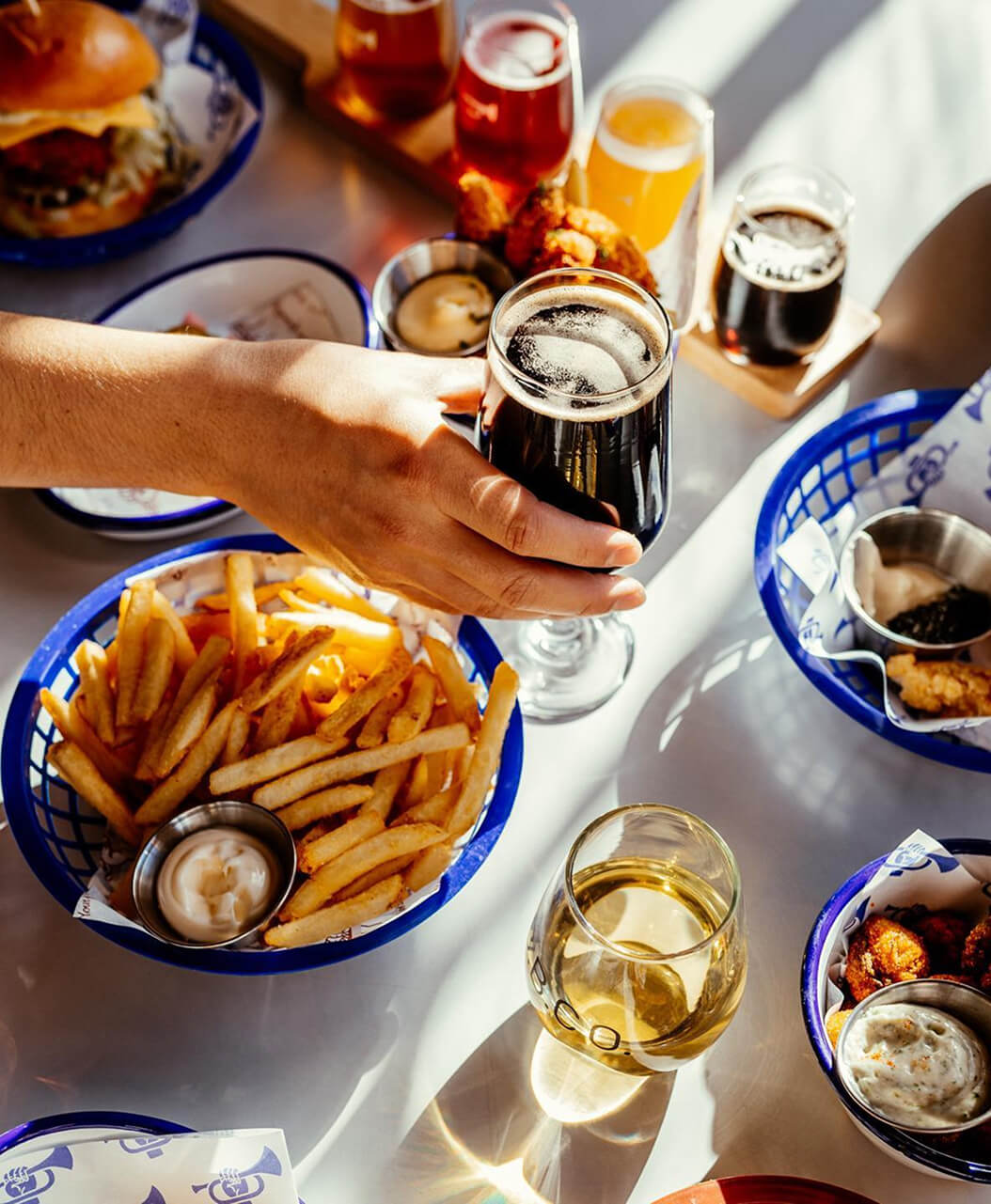 Hand holding a dark beer over a table with food and drinks. Brave brewing Co food for sharing