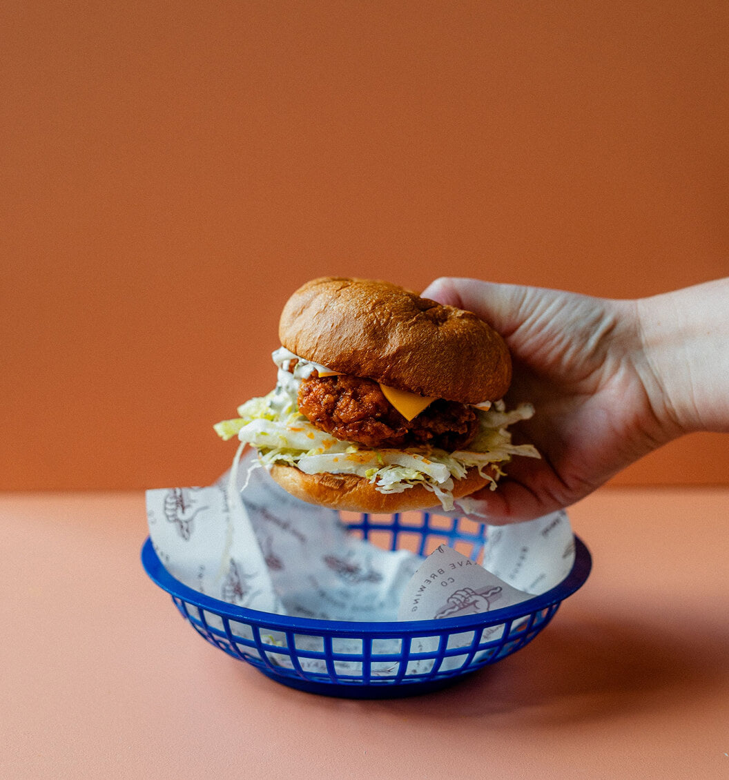 Hand holding a chicken sandwich with lettuce and cheese against an orange background