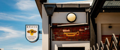 Brave Taproom & Eatery exterior with neon sign and logo against a blue sky.