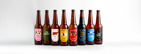 Row of eight beer Brave Brewing Co bottles with various labels on a white background