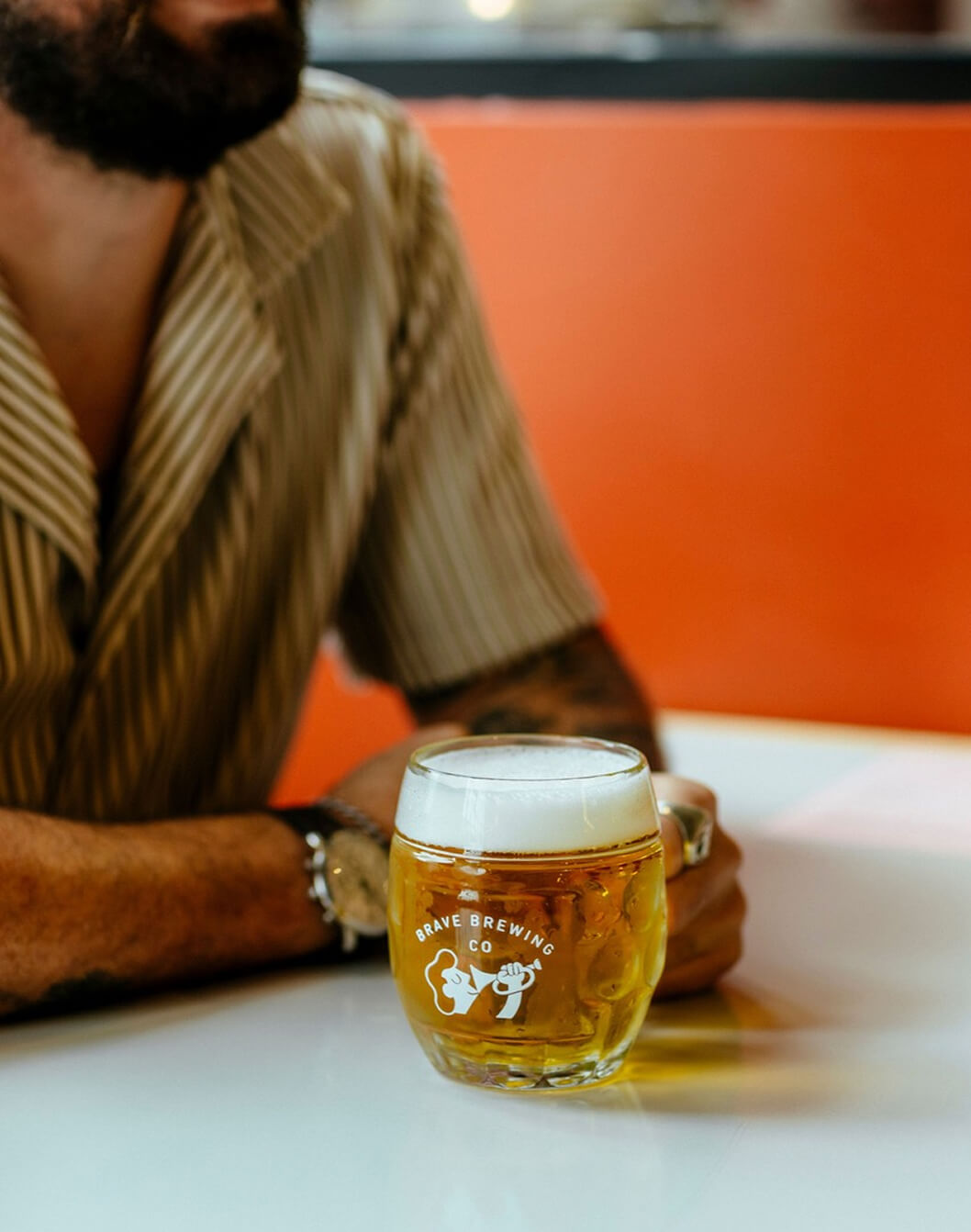 Person sitting at a table with a glass of beer featuring 'Brave Brewing Co.' branding.