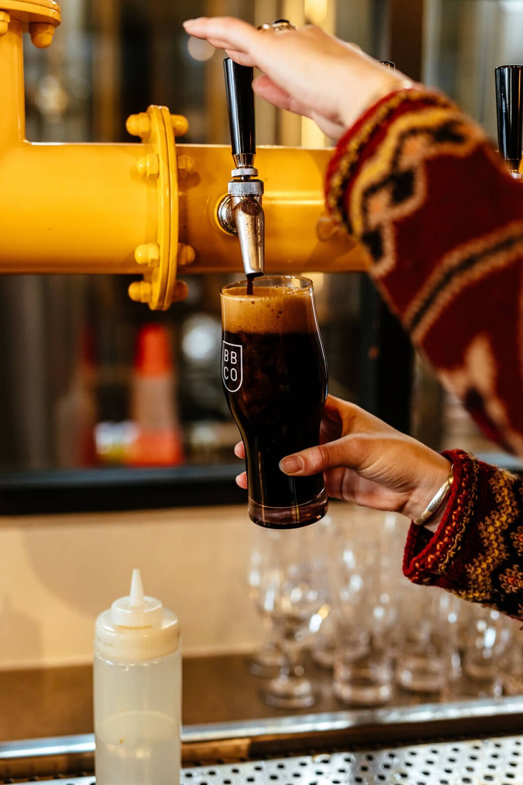 Person pouring a glass of Brave Brewing Co Milk Stout from a tap, with a blurred bar setting in the background.